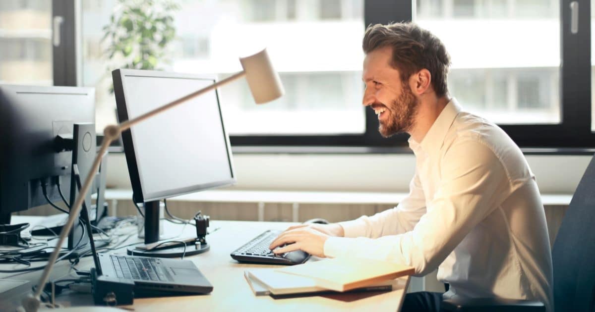 A man in white shirt who works in a creative sector smiles while working at a computer