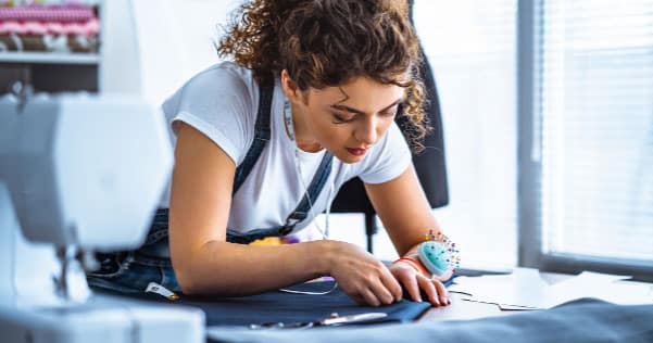 Woman wearing a pin cushion on her risk looking down at a garment that she is altering