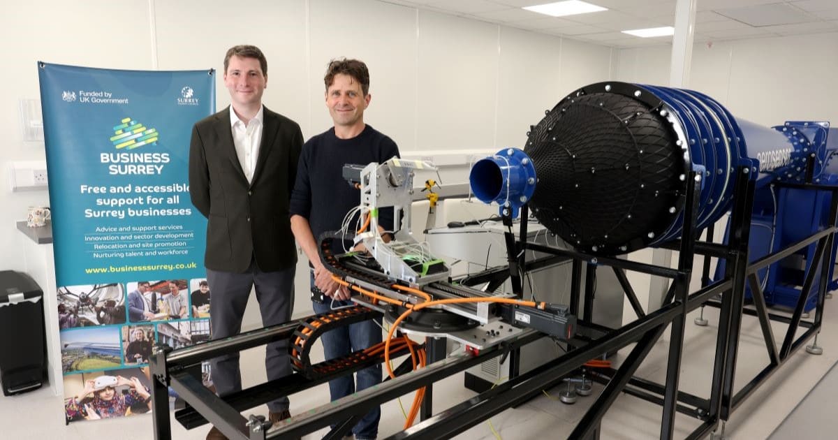 Two men stand behind a bright blue high tech piece of equipment with aerosensor written on it. Behind them is a banner for Business Surrey.