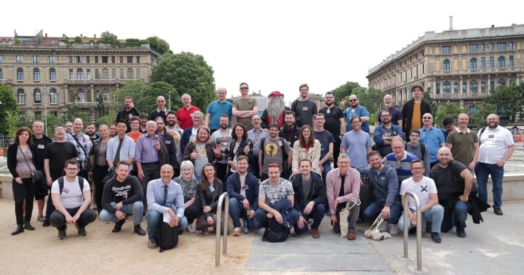 A group of people pose for an image while standing outside. Two historic buildings stand behind them.