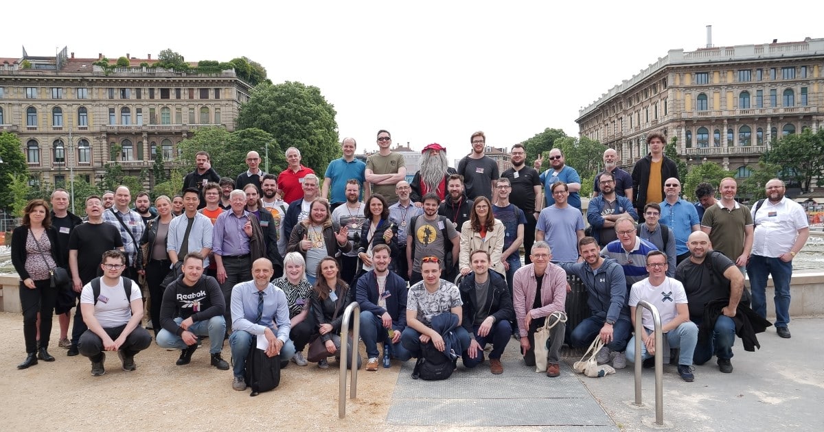 A group of people pose for an image while standing outside. Two historic buildings stand behind them.