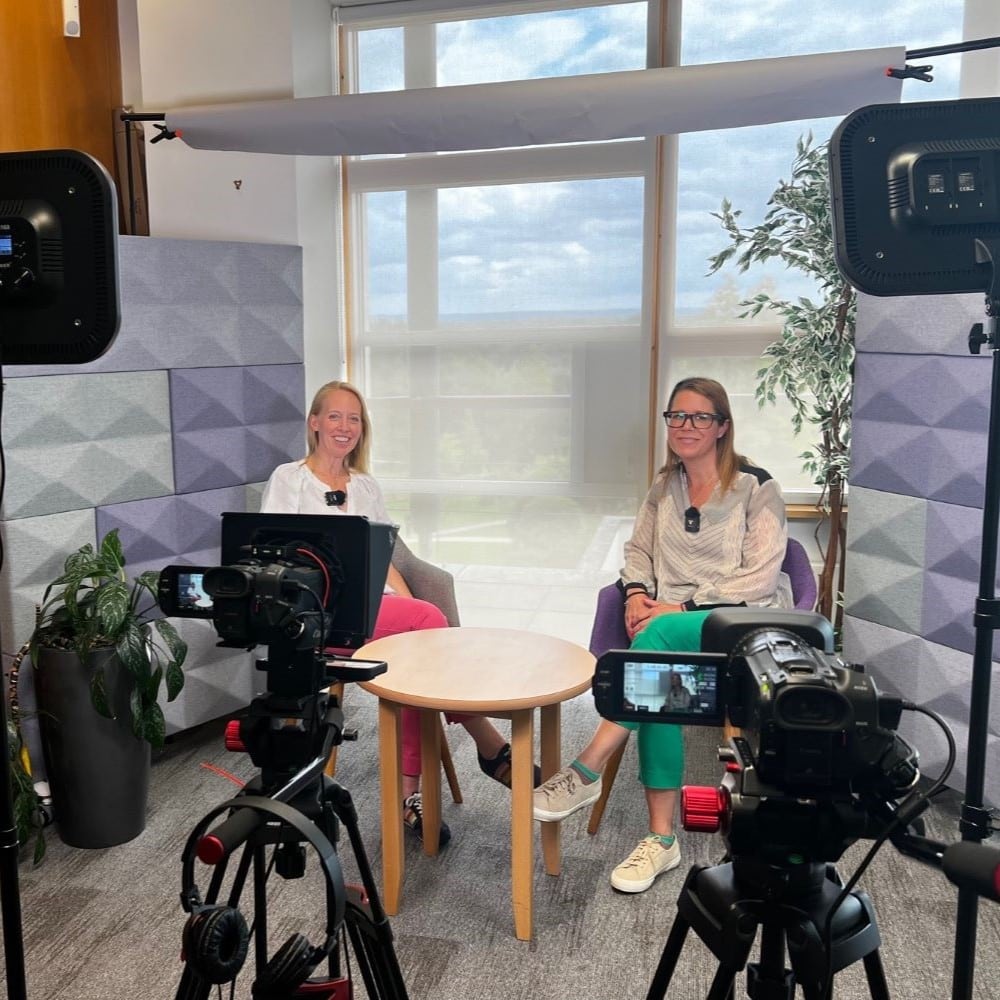 Square image of two women sat down in chairs during a multicamera filming production