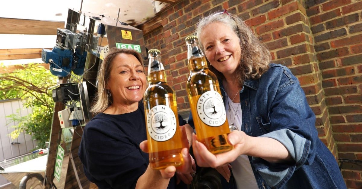 Two women smile while holding bottles of Misty Moon Cider, a drink made in Farnham, Surrey.