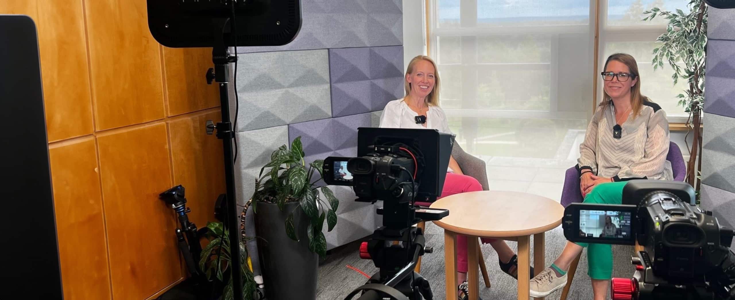 image of two women sat in chairs presenting a business toolkit. Two cameras are visible to the fore with lighting.