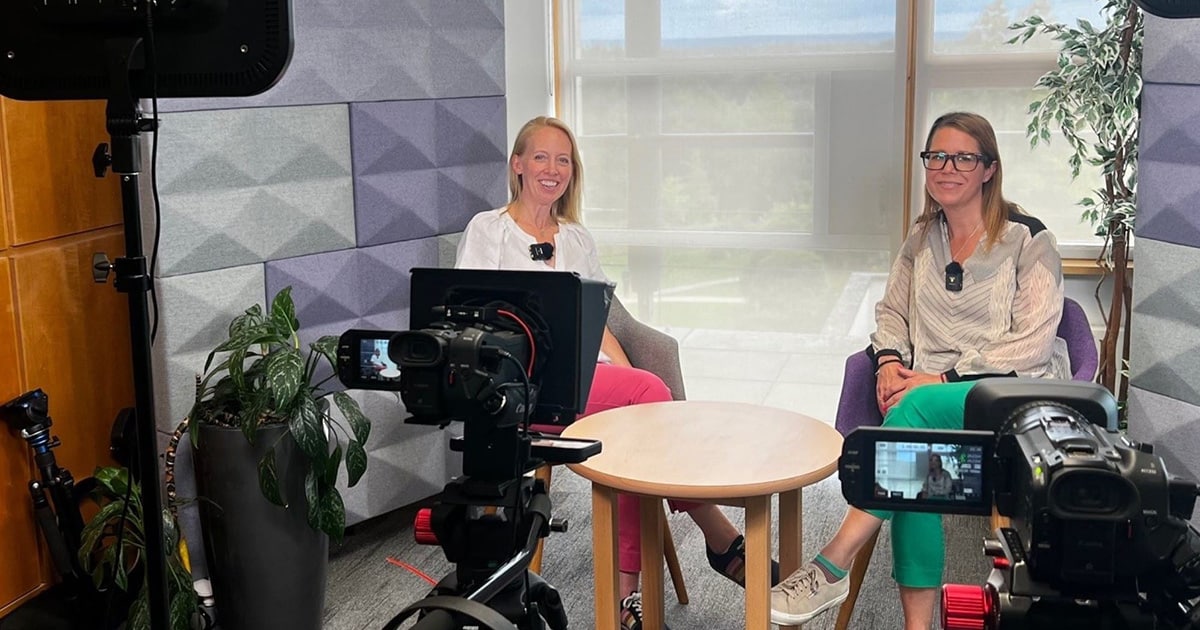 image of two women sat in chairs presenting a business toolkit. Two cameras are visible to the fore with lighting.