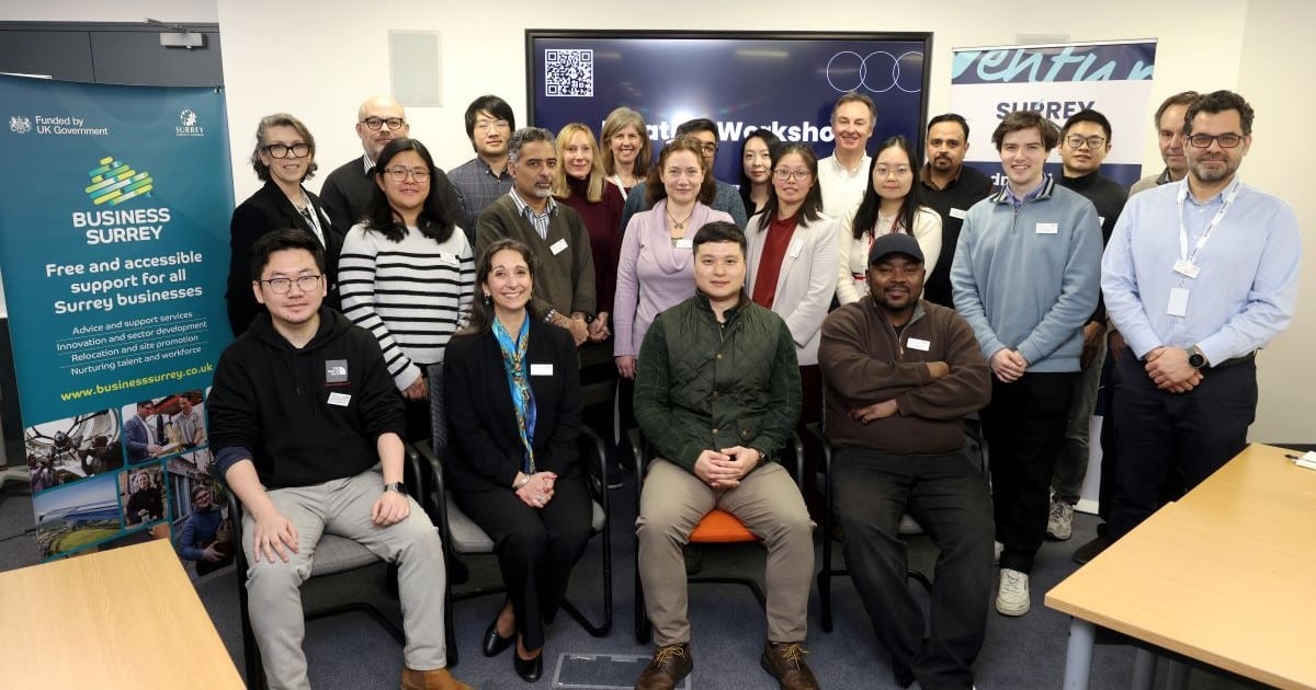 A group of people - some sitting and some standing - pose for a picture in front of promotional banners for Surrey Venture Studios and Business Surrey.