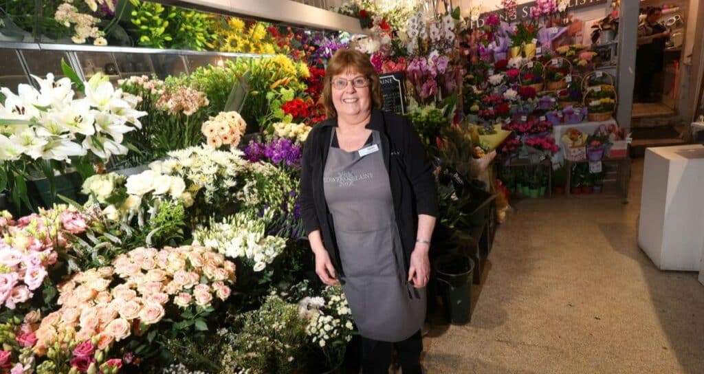 A high street florist smiles as she stands next to a colourful display of flowers in her shop