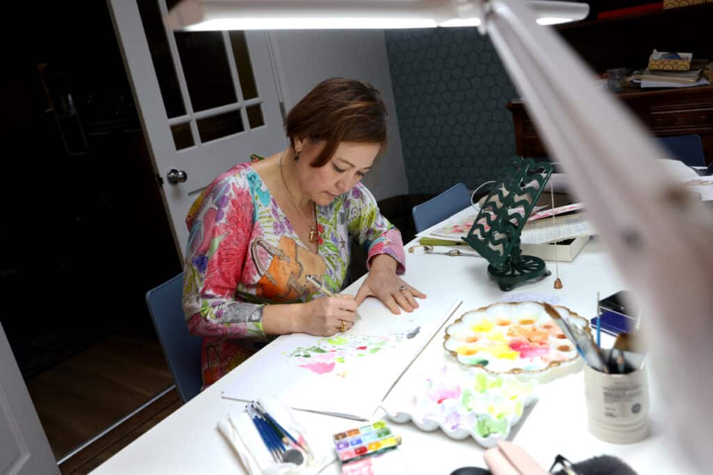 Kathy sits at a table working on her designs on paper. | Business Surrey, Economic Growth Fund