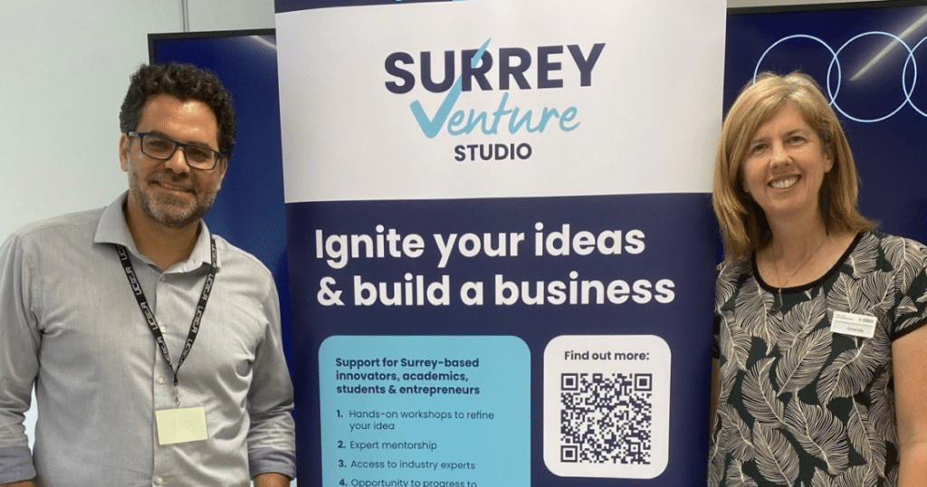 Surrey Venture Studio Accelerator - Amanda Lowe and Ody Bassioukas stand in front of a banner for SVS | Business Surrey |