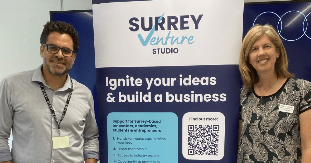 Surrey Venture Studio Accelerator - Amanda Lowe and Ody Bassioukas stand in front of a banner for SVS | Business Surrey | Surrey tech startups