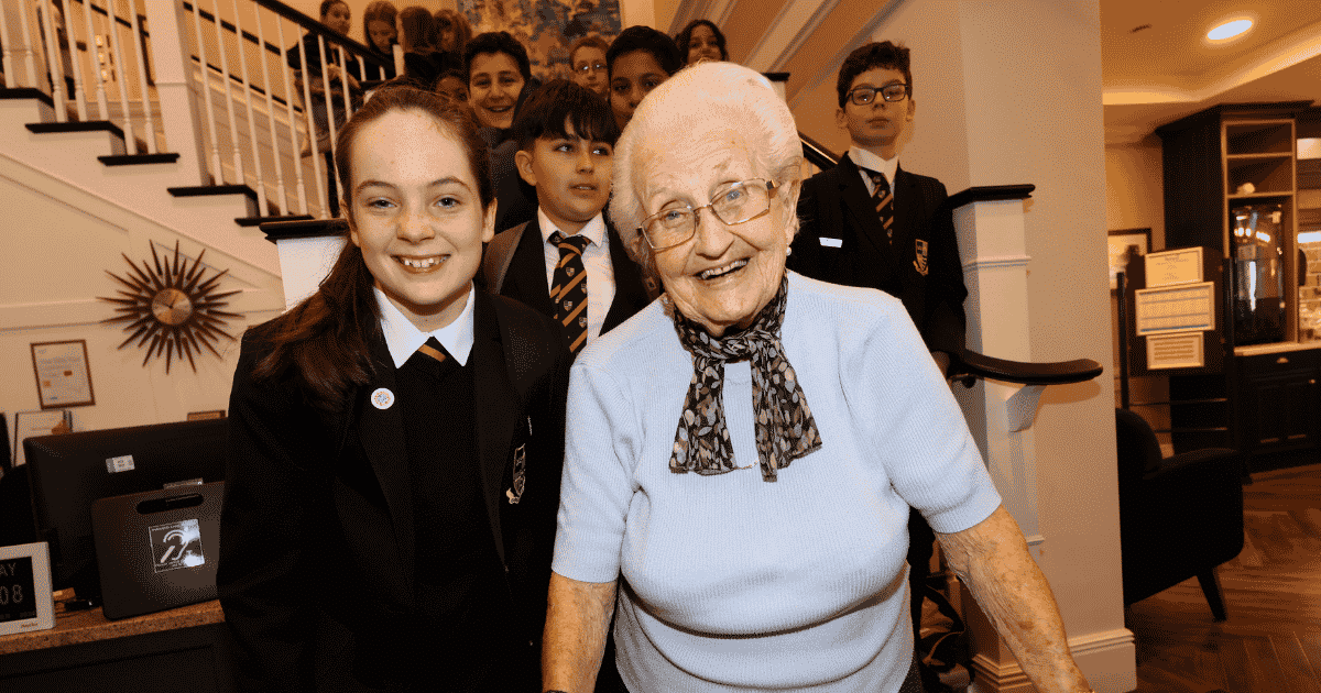 A school visit to a Surrey care home. students stand with a smiling elderly lady in a care home setting. | Surrey Careers Hub | Business Surrey | future workforce development